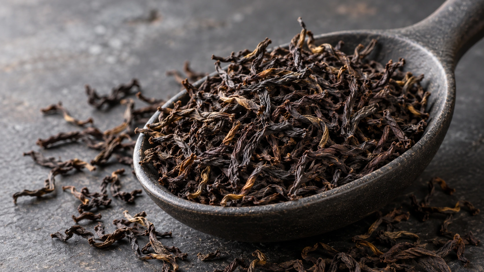 Original AI-generated editorial photograph of wiry Assam black tea leaves in a dark scoop