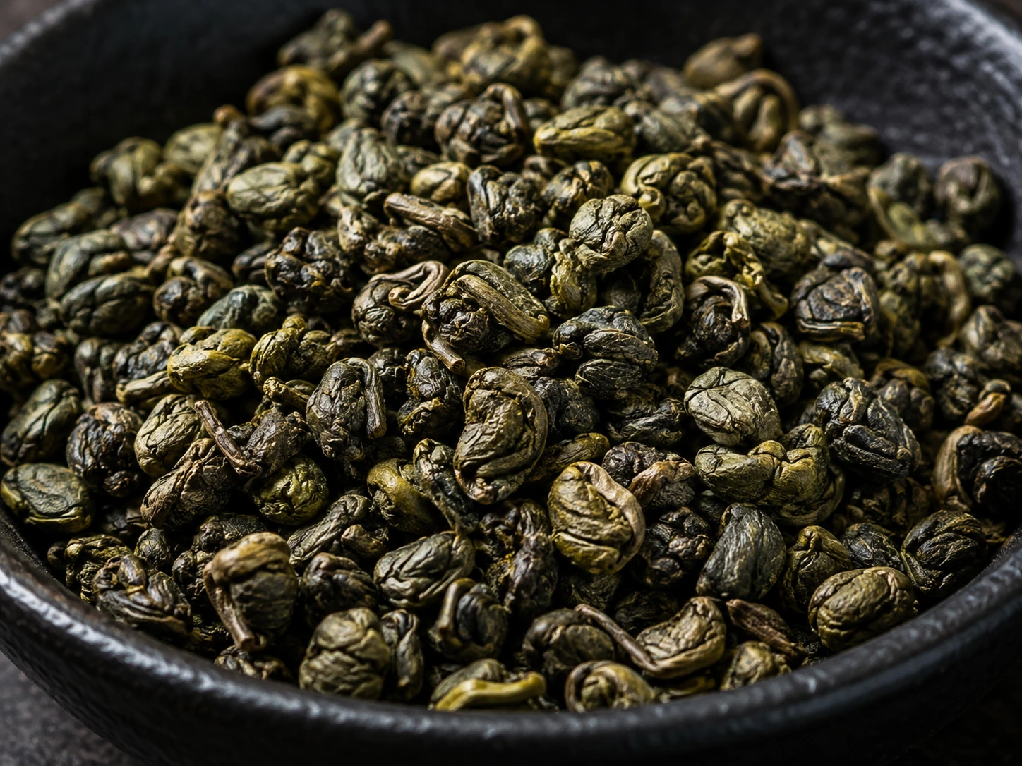AI-generated editorial photograph of tightly rolled pellets of gunpowder green tea; illustrative, not authenticated botanical or product evidence.