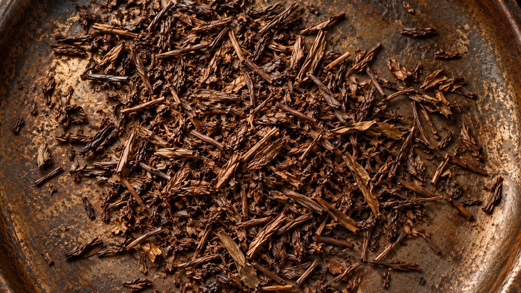 Original AI-generated editorial photograph of roasted brown hojicha leaves scattered on a patinated metal pan