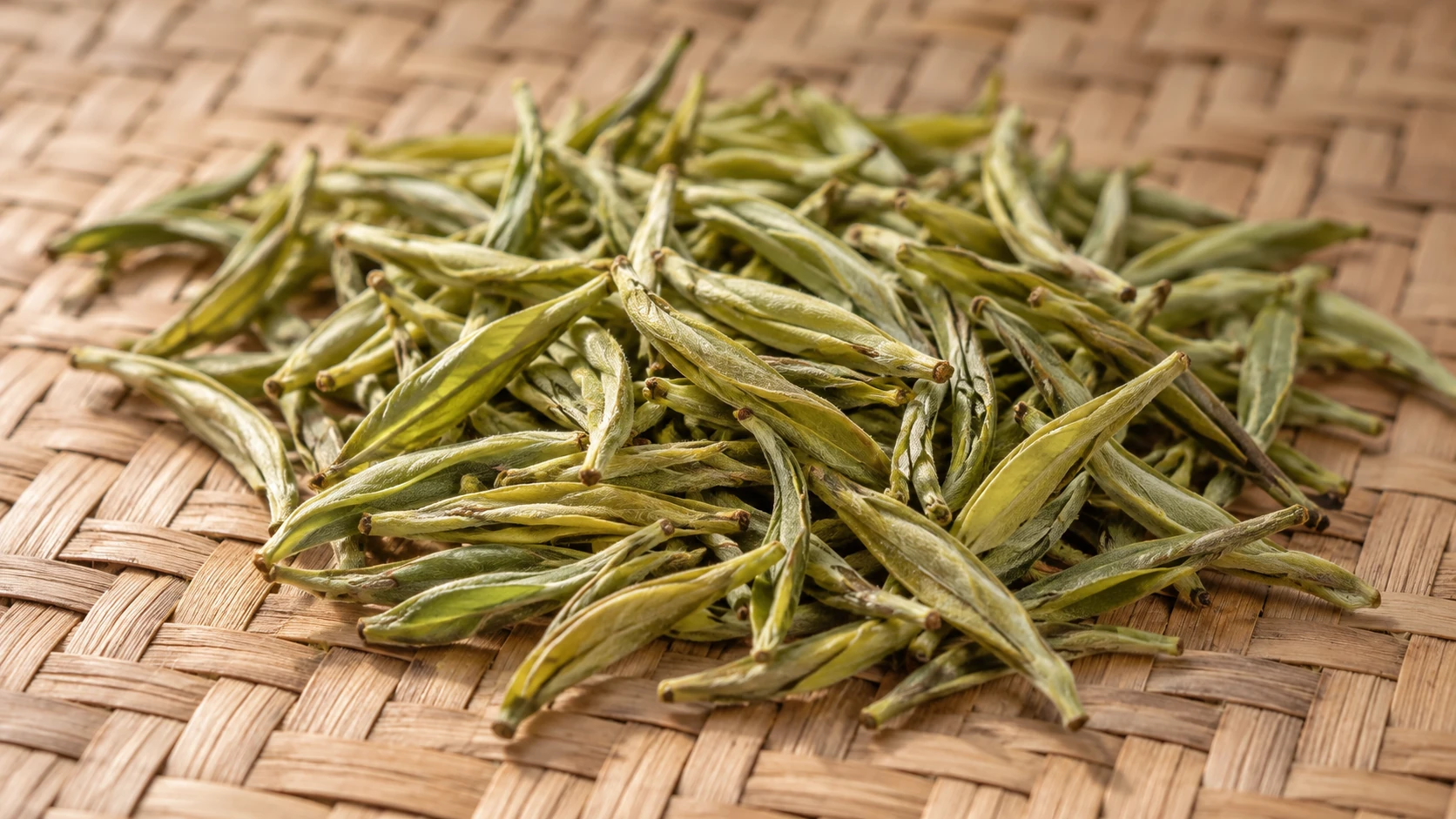 Pale yellow-green dried tea buds on a woven bamboo mat, illustrating yellow tea.