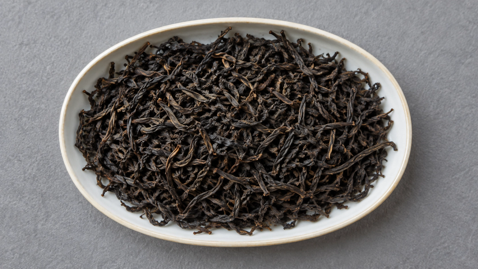 AI-generated editorial illustration: Dark dry twisted black tea leaves in a white oval dish; Keemun origin and cultivar unverified