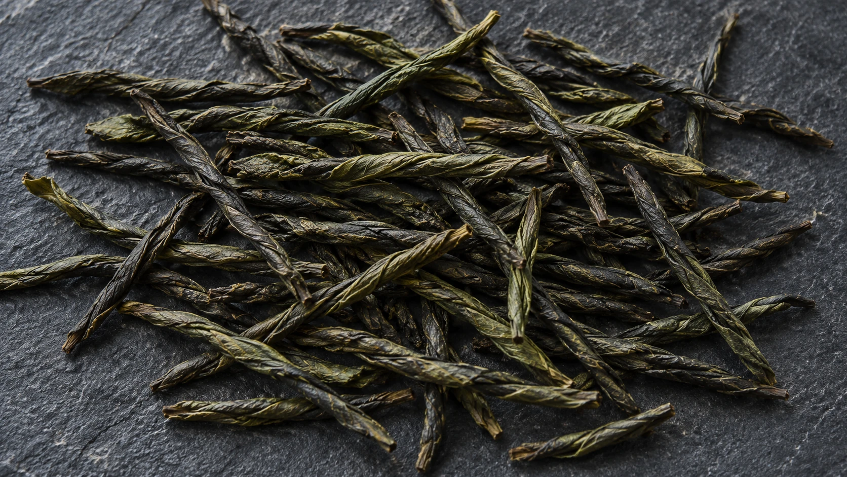 Dark twisted leaf strips on slate illustrating a bitter-leaf infusion.