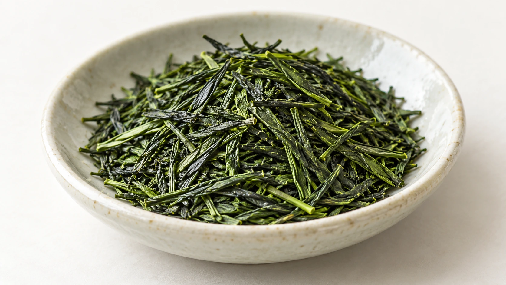 Original AI-generated editorial photograph of slender Japanese sencha leaves in a pale ceramic dish