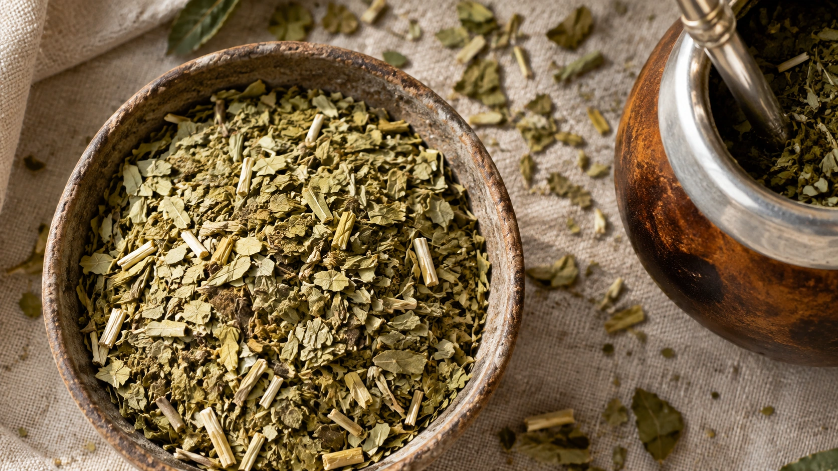 Original AI-generated overhead editorial photograph of chopped dried yerba mate leaves and stems beside a mate gourd with bombilla